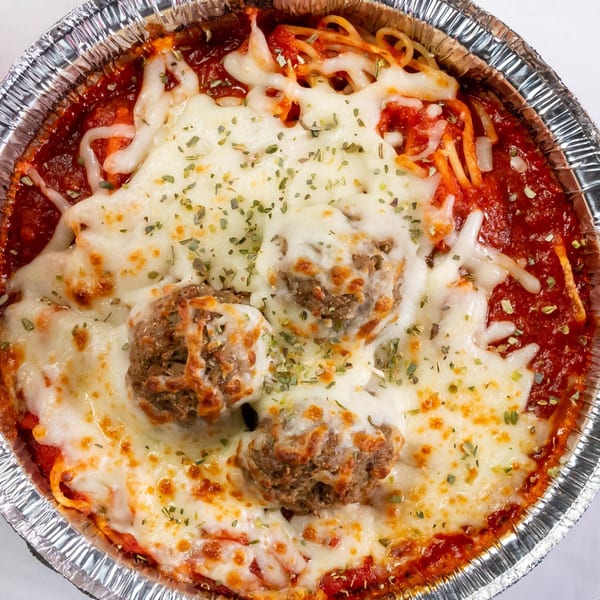 Baked spaghetti and meatballs with melted cheese and herbs in a foil container.