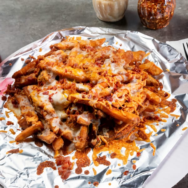 Grapevine Pizza & Cafe's cheesy bacon fries, served in aluminum foil, with chili flakes in the background.