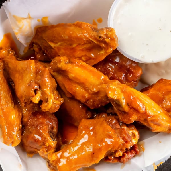 Close-up of Grapevine Pizza & Cafe's buffalo wings coated in orange sauce, with a side of ranch.