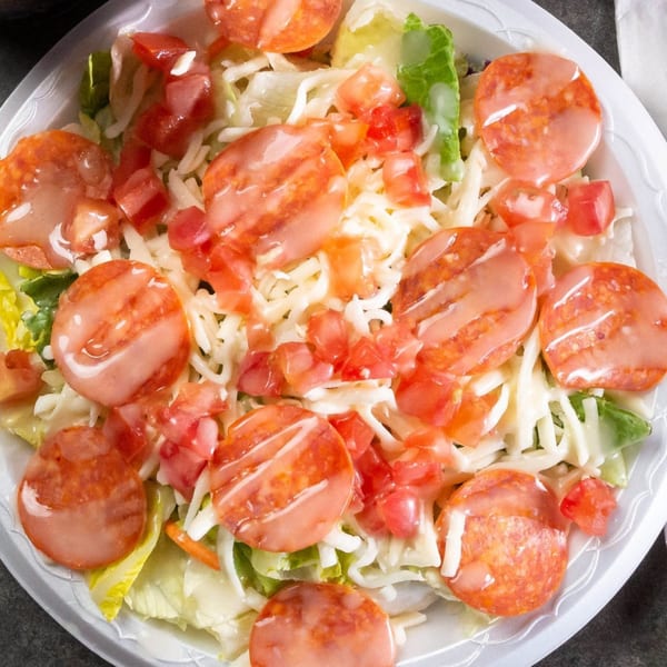A Grapevine Pizza & Cafe salad with pepperoni, shredded cheese, diced tomatoes, and dressing.