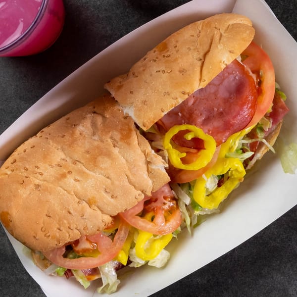 A Grapevine Pizza & Cafe sub sandwich with salami, lettuce, tomatoes, and banana peppers.